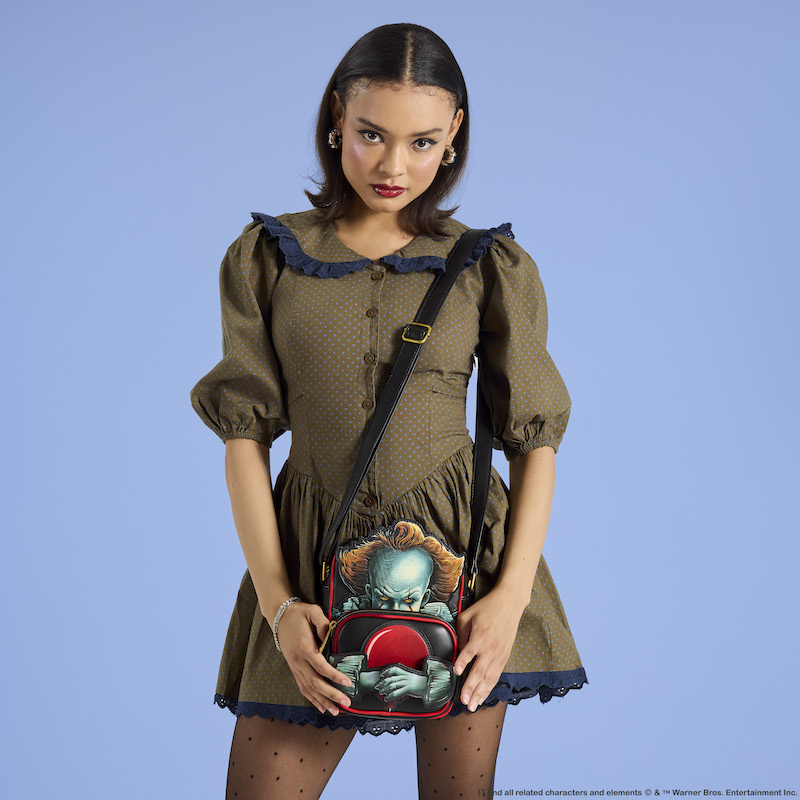 Woman wearing a dress, standing against a light blue background, wearing the Loungefly Pennywise Crossbuddies Crossbody Bag over a shoulder. 
